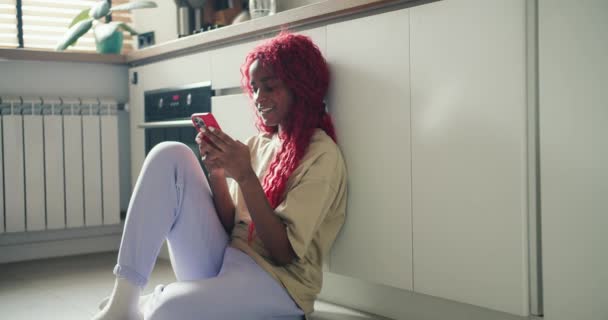 Kırmızı Kıvırcık Saçlı Neşeli Afro Amerikalı Kız Mutfak Zemininde Oturuyor — Stok video