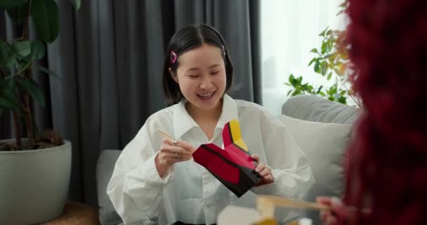 若いですアジアの女性で良い気分食べる麺とともに木棒とともに自宅で彼女の友人 — ストック動画