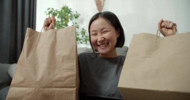 Heyecanlı Asyalı kadın internetten alışveriş yapıyor, evde hediye çantalarını kafasının üstüne kaldırıyor..