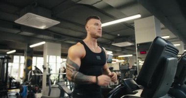 Dövmeli genç bir adam koşu bandında koşuyor. Spor salonunda ısınma, kardiyo..
