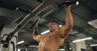 Spor salonunda barfiks çeken çıplak gövdeli genç bir sporcunun yan görüntüsü..