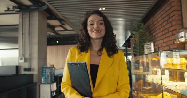 穿着黄色夹克衫的自信快乐的女商人拿着笔记本走进办公室 — 图库视频影像