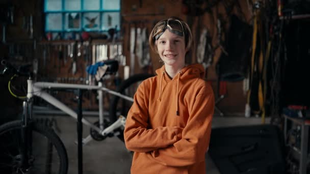 現代の製造業の精度 10代の専門知識 ワークショップを背景に ゴーグルとオレンジのスウェットシャツを着た10代の若者がポーズをとる — ストック動画