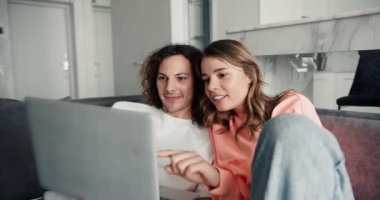 Sevgi dolu genç bir çift dizüstü bilgisayara bakıyor, tatil planları yapıyor, internette sörf yapıyor, kanepeye kıvrılıyor..