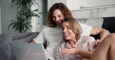 Yüzünde kalp etiketi olan komik bir çift internette video görüşmesinde konuşuyor, evdeki kanepede dizüstü bilgisayar kullanarak oturuyor..