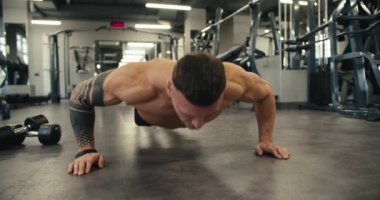 Güçlü atletik adam spor salonunda üstsüz antrenman yapıyor, şınav çekiyor. Spor salonunda spor yaparken kaslı sporcu sağlıklı kalıyor. Terleme ve kararlılık başarıya götürür..