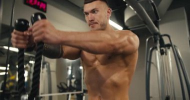 Dikey sıra makinesi, eller ve sırt egzersizleri yapan yakışıklı bir genç. Spor tesisleri, arka planda spor yapan erkek ve kadın..
