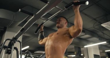 Spor salonunda barfiks çeken çıplak gövdeli genç bir sporcunun yan görüntüsü..