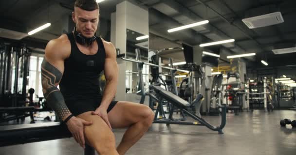 一名身穿黑色T恤衫的年轻运动员在健身房又做了一次运动后 正在按摩他的腿 — 图库视频影像