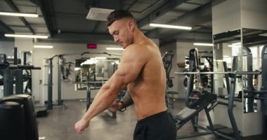 Çıplak gövdeli genç bir sporcu poz verir ve kaslarını gösterir. Spor salonunda uzun ve sıkı çalışmanın sonucu..