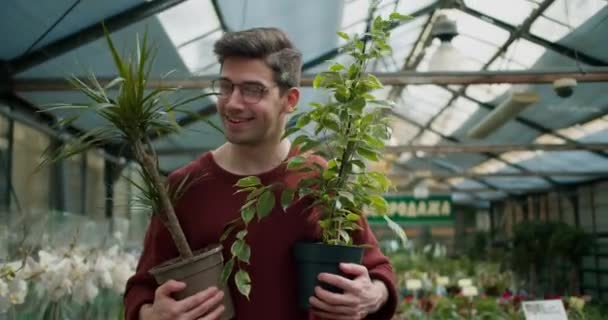 植物学者の閲覧 若い男のショッピングアドベンチャー 2つの花を持つ若い男が専門の花屋を通って歩く — ストック動画