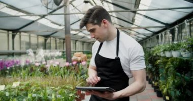Bir Çiçek Dükkanında Teknoloji-Tasarruf Envanter Yönetimi. Siyah önlüklü genç bir adam özel bir mağazanın çalışanı olarak çiçeklerin listesini yapar..