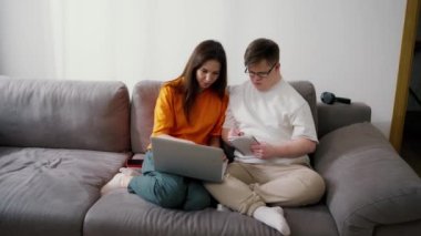 Down sendromlu bir adam evde öğretmeniyle ya da kız kardeşiyle birlikte dizüstü bilgisayardan notlar yazıyor..