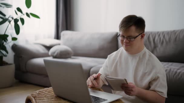 ダウン症候群の若い大人の男が家に座って 学習のためのラップトップを使用して — ストック動画