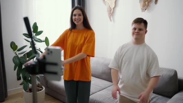 年轻的唐斯综合症患者与一对微笑的女孩在家里的前部移动摄像机前跳舞 — 图库视频影像