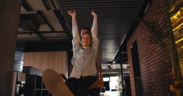 ダイナミックオフィスの楽しさ 喜びと笑いをオフィスチェアでブルーブルースローリングのブルネットの男とブロンドの女の子 — ストック動画