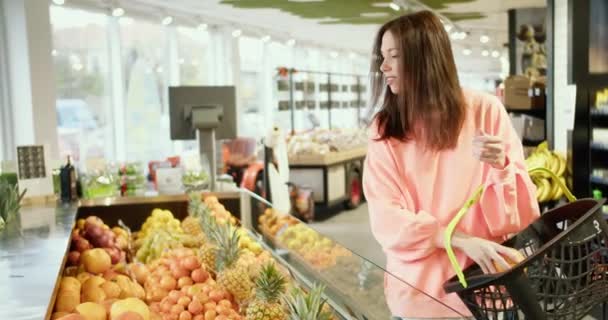 楽しい柑橘類の選択 ハッピーブルネットの女の子はスーパーマーケットで果物を選ぶ — ストック動画