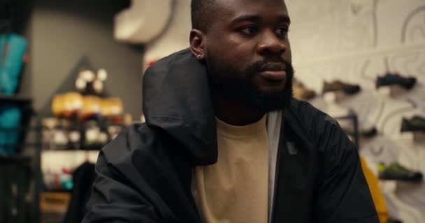 詳しく見る 屋外ギア店で黒いウインドブレーカーを試してみるアフリカ系アメリカ人の男 — ストック動画