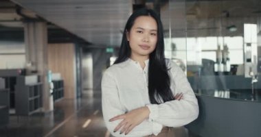 Ofisin arka planına karşı beyaz gömlekle poz veren kendine güvenen Asyalı kız. Başarıya giden yol.