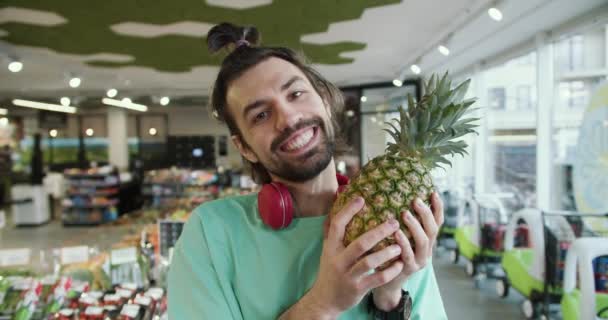 遊び心のあるパイナップルの楽しみ スーパーマーケットで緑のTシャツの若い男ヒラリーアニックス — ストック動画