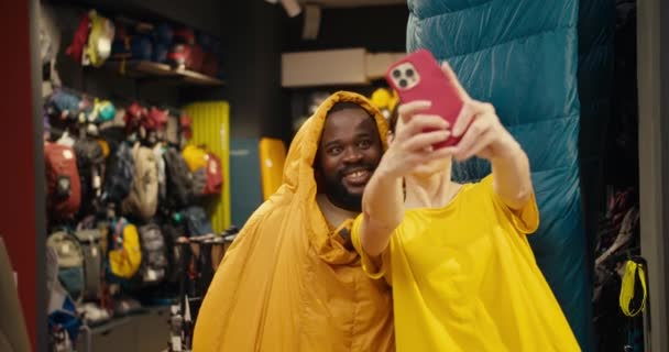 笑いと遊び心 ハイキングギア店での黒人男性とヨーロッパの女の子の思い出に残るセルフィーセッション — ストック動画