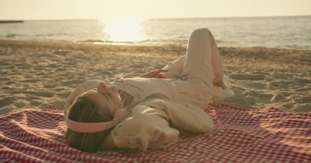 Блондинка Легкому Одязі Рожеві Навушники Слухає Музику Лежить Упаковці Сонячному — стокове відео