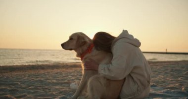 Sarışın kız sabah kumsalda köpeğini okşuyor. Güneşli bir sabah, güzel bir güneş ışığı transfüzyonu..