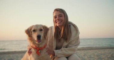Genç sarışın bir kızın portresi köpeğini okşuyor ve sabahları sahilde kameraya bakıyor..