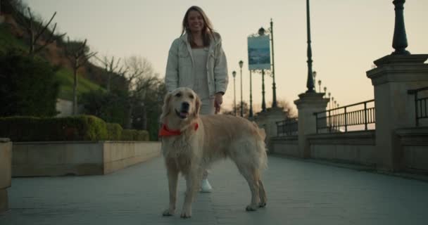 夜明けに堤防の背景にポーズをとっている若い女の子と彼女の光色の犬の肖像 — ストック動画