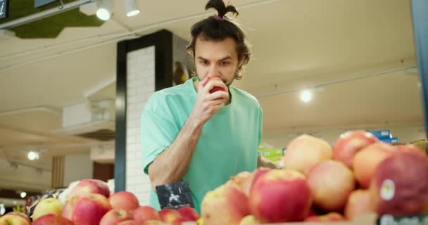 フレッシュアップルセレクション グリーンセーターの若者がスーパーでジュースイエローレッドアップルを選ぶ — ストック動画