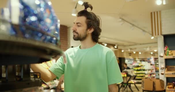 効率的なショッピング グリーンTシャツの男はスーパーマーケットでバスケットにアイテムを選択して追加します — ストック動画