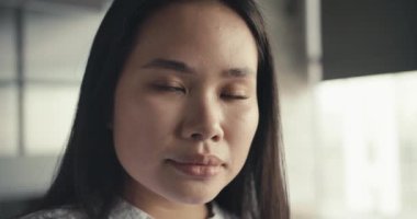 Ofisin arka planında beyaz gömlekli Asyalı esmer bir kızın portresi. İş kızı genç kız kameraya bakıyor..