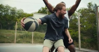 Gri tişörtlü bir adamın, basketbolda beyaz tişörtlü arkadaşının yanından geçerken, parlak bir gol attığı ve başarısından çok mutlu olduğu yakın plan bir fotoğraf..