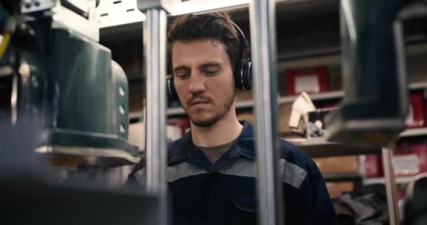 在一家服装厂 一个戴着黑色耳机的红头发男子在一台工业机器上工作的特写镜头 以优质胶卷拍摄 — 图库视频影像