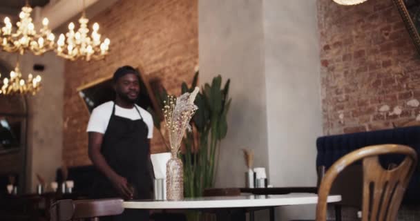 一个穿着黑色围裙和白色T恤的黑人在餐馆的桌子上放了一个预订的标志 餐厅预订餐桌 — 图库视频影像
