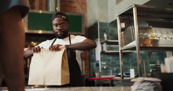 黒人はドナー市場の訪問者にサービスを提供しています 男は客に紙袋を注文する 環境への配慮 — ストック動画