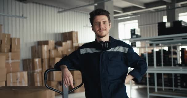 一个身穿蓝色制服的男人微笑着看着摄像机 靠着一台特殊机器的手柄 靠着一家工厂仓库的后面 — 图库视频影像