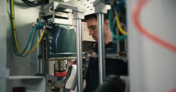 一个身穿蓝色制服 头戴黑色耳机的男人站在工厂机器后面 确保机器正常运转 — 图库视频影像