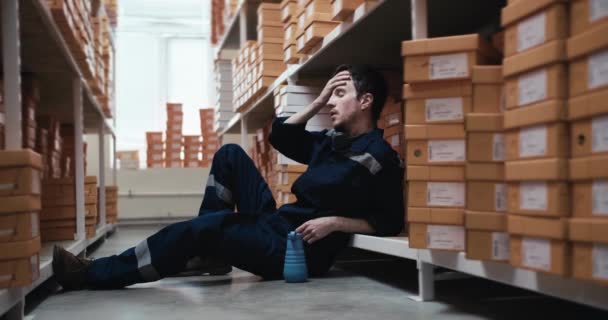 一个身穿蓝色制服 身穿黄色盒子的疲惫男子坐在地板上 喝着瓶子里的水 工作休息 工作日累人 — 图库视频影像