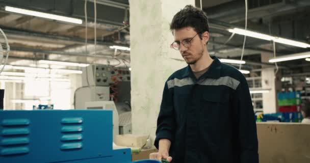 ガラスの男と青い制服は 工場を背景に靴の生産のための特別なマシン上で動作します — ストック動画