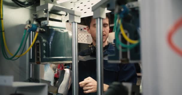 青い制服の男が工場の機械の後ろに立ち 機械を適切に操作する方法について従業員からアドバイスを受ける 織物工場でのインターンシップ — ストック動画