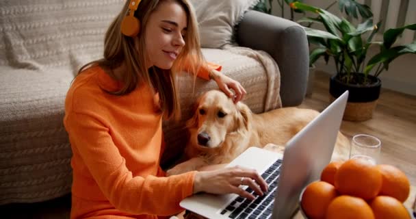 Zbliżenie Blondynka Pomarańczowym Swetrze Żółtych Słuchawkach Pisze Laptopie Głaskając Swojego — Wideo stockowe