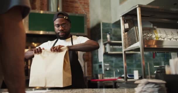 黑人在捐赠市场上为游客提供服务 一个男人用纸袋向顾客下订单 对环境的关注 — 图库视频影像