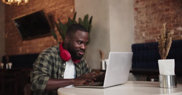 Ένας Μαύρος Χαρακτήρας Γενειάδα Κόκκινα Ακουστικά Δουλεύει Συναισθηματικά Ένα Λάπτοπ — Αρχείο Βίντεο