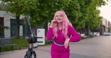 Pembe elbiseli ve pembe saçlı mutlu bir kız kanalı için bir video blogu hazırlıyor. sokak video çekimi.