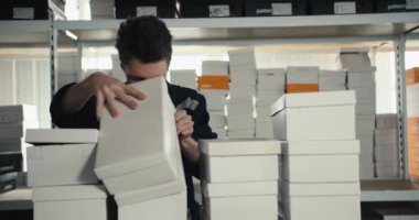 Mavi üniformalı ve gözlüklü kızıl saçlı bir adam depodaki tüm kutuların varlığını kontrol ediyor. Yüksek kalitede çekilen video.