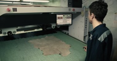 Özel üniformalı bir adam giysi fabrikasında lazer makinesiyle doğru malzemeyi kesiyor. Yüksek kalitede çekim.