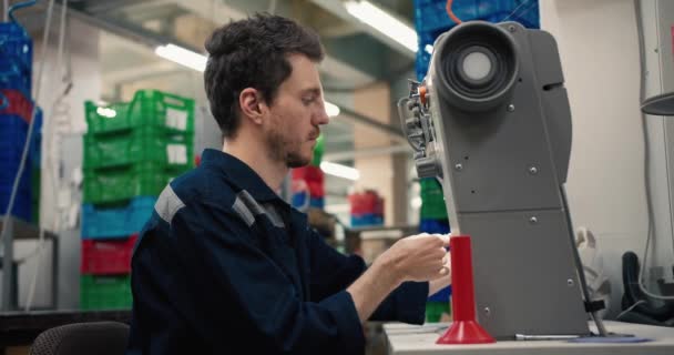 一个红头发的男人穿着蓝色制服在纺织厂的缝纫机上工作 一个人在一台特殊的机器上缝制一块布料 — 图库视频影像