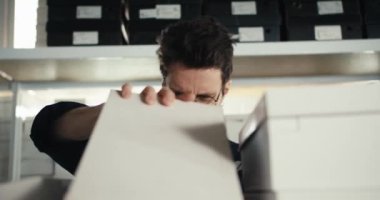 Mavi üniformalı ve gözlüklü kızıl saçlı bir adamın depodaki tüm kutuları kontrol ederken yakın plan fotoğrafı. Yüksek kalitede çekilen video.