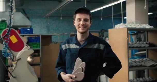 一个身穿蓝色制服 头戴帽子的男人手里拿着鞋垫 在一家纺织厂的背景下摆姿势 鞋厂工人肖像 — 图库视频影像
